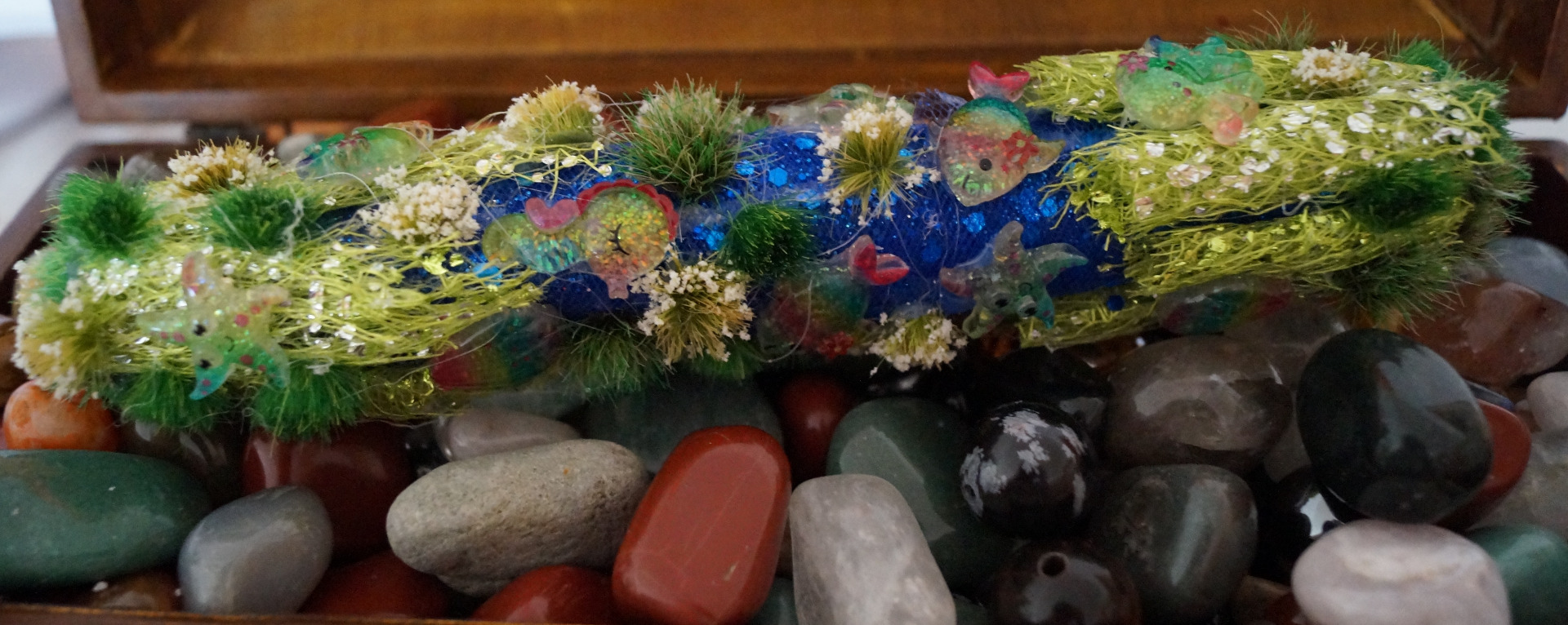 Holzstab 20 cm lang, Wachs, Glitterstoff dunkelblau und hellgrün, künstliche kleine Rasenstücke grün, mittelgrün und weiß, 14 kleine Meeresbewohner aus Harz, wie Fische, Seesterne, Seepferdchen, Muscheln u.a.