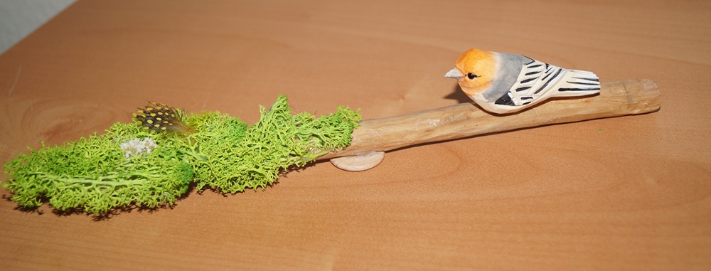 Treibholzstab ca. 27 cm lang, bearbeitet und geschliffen, Wachs, künstliches Gras, 1 kleine bunte Feder, 1 weißes Grasbüschel, 1 Holzvogel mit Schnabel ca. 7 cm, 1 kleines Stehplättchen