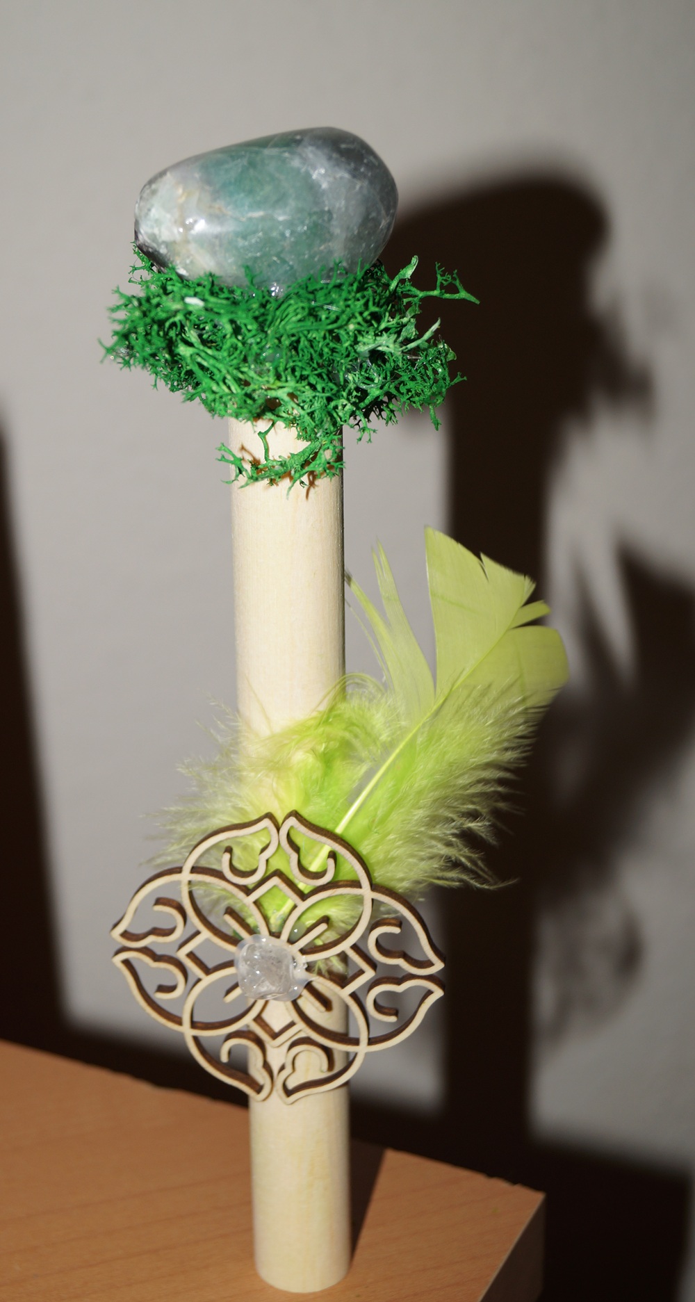 Holzstab 20 cm lang, 1 hellgrüne Feder, 1 Holzornament 6 cm, 1 Bergkristall 1 cm, 1 Flourit 4 x 2,5 cm, künstliches Gras, Wachs