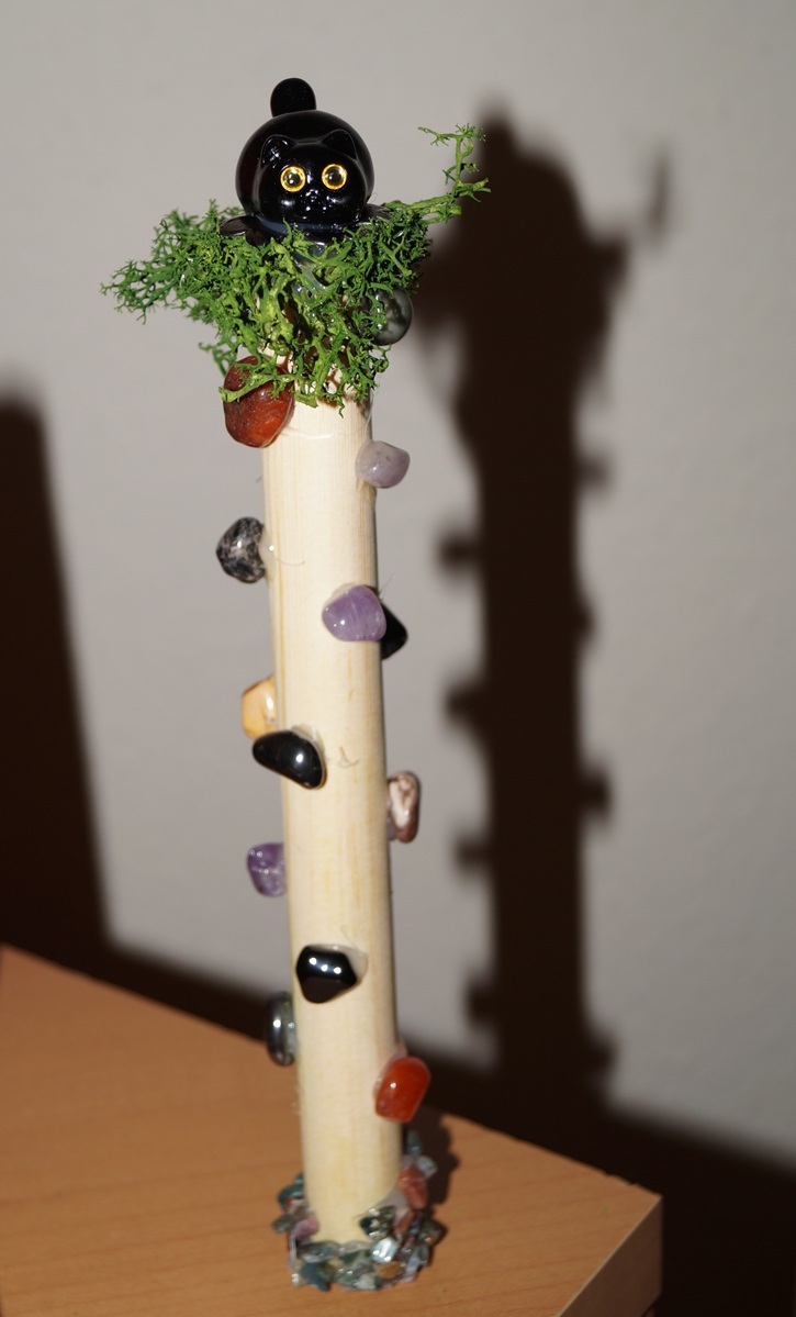 Holzstab 20 cm lang, Wachs, künstliches Gras, Sockel mit verschiedenen Edelsteinsplitter, 1 schwarze Katze 3 x 2 cm, 1 Metallblüte Durchmesser ca. 3cm, 15 Edelsteine zwischen ca. 0,8 - 1,5 cm- Hämatit, Landschaftsjaspis, Carneol, Amethyst, roter Jaspis, Apachenträne